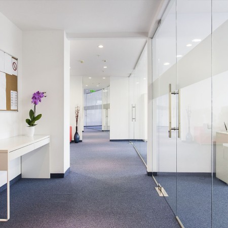 Moderner Büroraum mit blauem Teppichboden und großen Glastüren entlang des Flurs